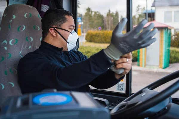 Maskeli otobüs şoförü, kendini koronavirüs salgınından korumak için otobüste eldivenlerini takıyor.