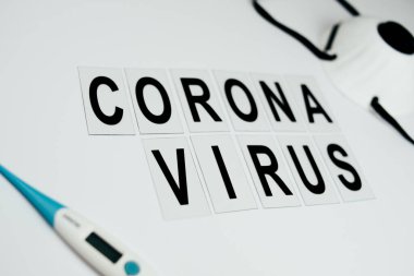 Beyaz arkaplan ve beyaz arkaplandaki metin için termometre ve maske üzerindeki siyah yazıt koronavirüsü