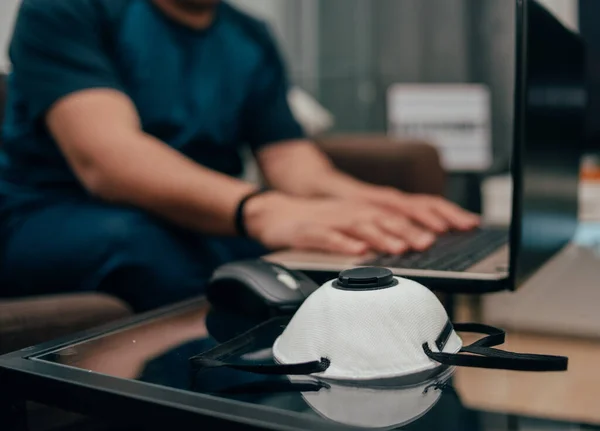 man works from home to avoid harming other people\'s dangers. close up photo of protective mask  lies near the laptop. young hispanic man sitting on couch and working at computer. man working online during quarantine.