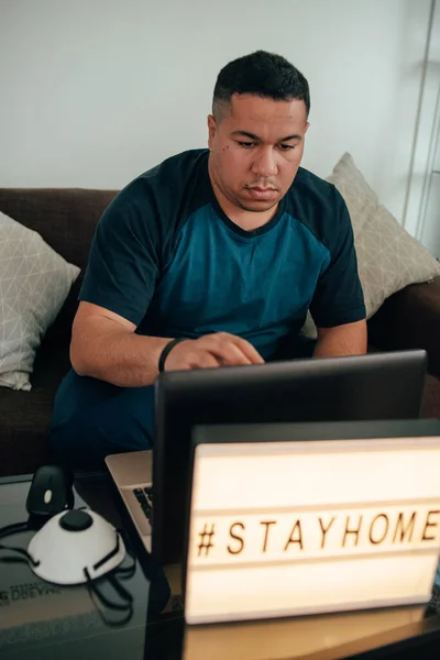 Kanepede oturan ve karantina sırasında bilgisayar başında çalışan genç bir İspanyol. İnsan, başkalarının tehlikelerinden kaçınmak için evden çalışır. Koruyucu maske ve eldivenler dizüstü bilgisayarın yanında. Genç İspanyol adam, Coronavi 'nin yayılmasını nasıl durduracağını düşünüyor.