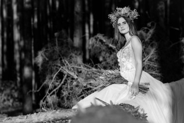 Şık buketi ve çelengi olan muhteşem, mutlu esmer gelin. Arka planda güzel bir orman manzarası. Doğal makyaj, saç stili, çelenk. Ormanda bir buket kurumuş çiçekle gelin. siyah ve beyaz