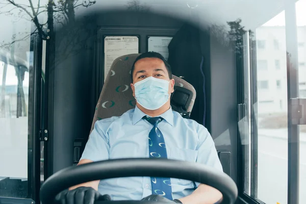 Maskeli sürücü araba sürerken yola bakar. Corona virüsü kavramı. Mavi tişörtlü genç latin otobüs şoförü ellerinde mavi tıbbi koruma maskesi ve siyah eldivenleri var. Otobüs şoförü covid 19 enfeksiyonunu önlemek istiyor.