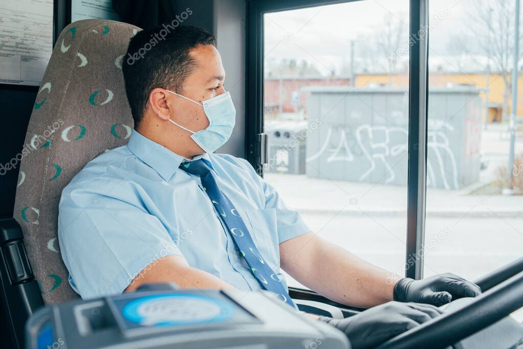 young hispanic man bus driver has blue medical protection mask and black  gloves on hands to protect himself from covid 19. driver in mask looks at the road.