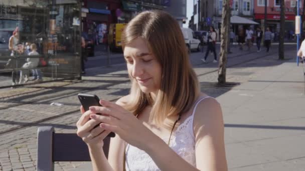 O tânără studentă își petrece timpul liber în oraș, folosind smartphone-ul — Videoclip de stoc