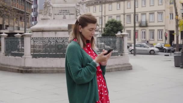 Jonge vrouw toerist staat op het stadsplein, met behulp van haar mobiele telefoon — Stockvideo