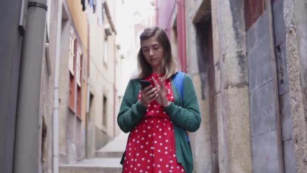 年轻的女游客正站在一条狭窄的老街，用她的手机 — 图库视频影像