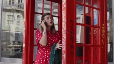 Kırmızı telefon kulübesinde dikilen, cep telefonuyla konuşan bir kadın