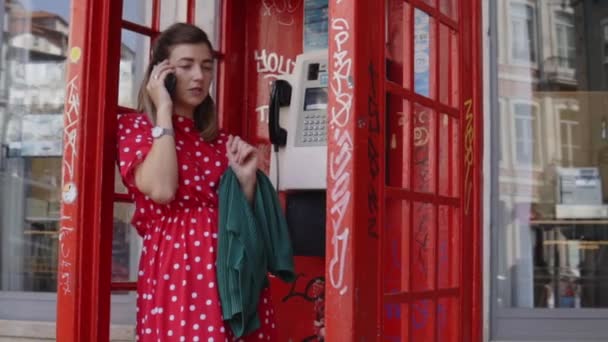 Mujer joven está hablando en su teléfono inteligente, de pie en la vieja caja de teléfono rojo — Vídeos de Stock