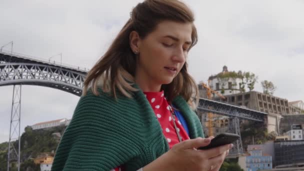 Fiatal nő, a diák a folyóparton sétál, használja a mobilját. — Stock videók