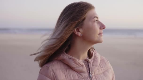 Junge brünette Frau, die abends am Strand steht und auf den Ozean blickt — Stockvideo