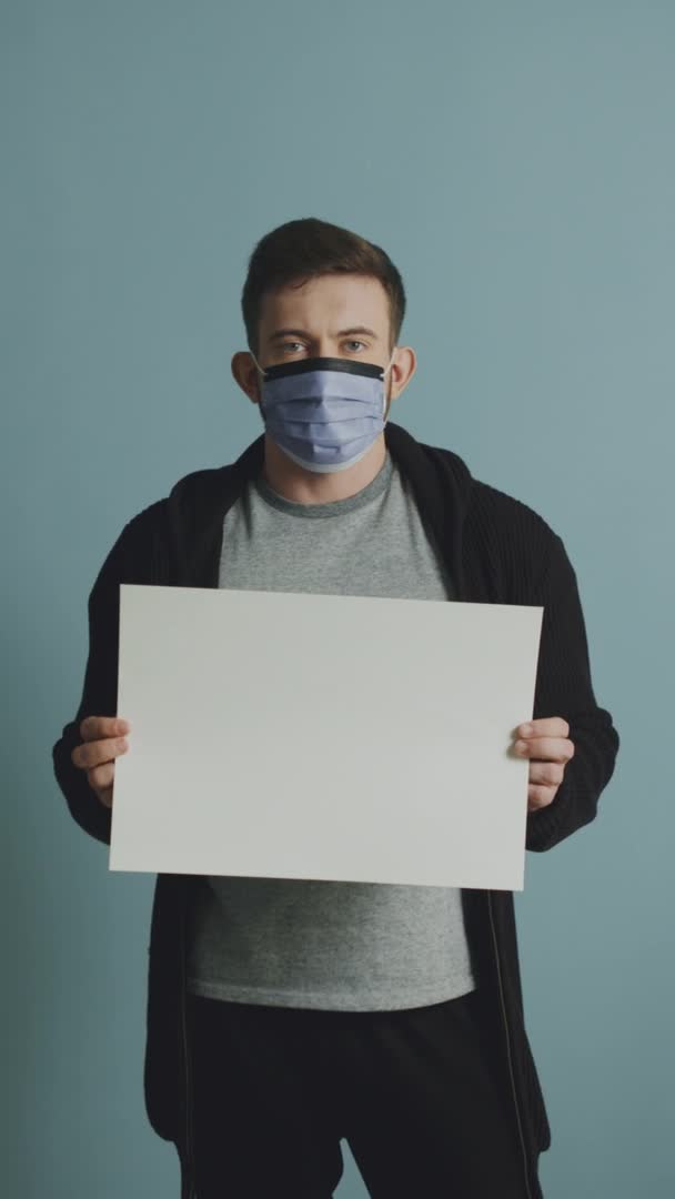 Jongeman in beschermend masker houdt een wit vel papier vast — Stockvideo