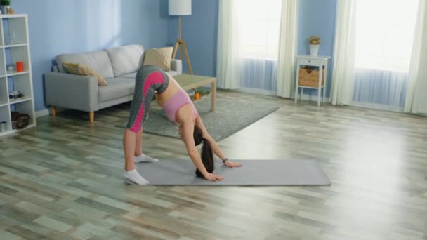 Mujer joven practica yoga matutino, con auriculares inalámbricos — Vídeos de Stock