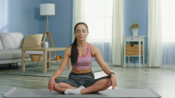 Jovem mulher está sentada no tapete de fitness e relaxante — Vídeo de Stock