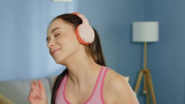 Jovem feliz mulher está ouvindo música no fone de ouvido rosa — Vídeo de Stock