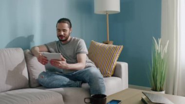 Genç adam evdeki koltukta oturuyor, internetten iletişim kuruyor.