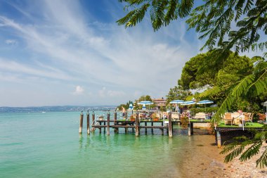 Güneşli sahil tropikal Cafe pier Sirmione'da Garda Gölü, Lombardia bölgesi, İtalya ile görünümünü.