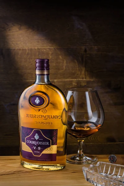 MOSCOW, RUSSIA - 15 Aralık 2018: Courvoisier konyak şişesi, bir bardak içki ve sigara ahşap masa. Courvoisier dünyadaki en popüler dört konyak markasından biri..