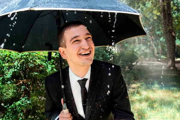 Fiatal férfi fekete öltöny napos eső nap égisze alatt — Stock Fotó