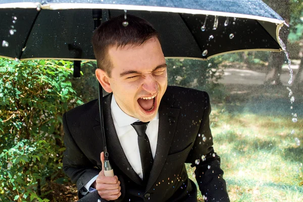 Jovem de terno preto em dia chuvoso ensolarado sob guarda-chuva — Fotografia de Stock