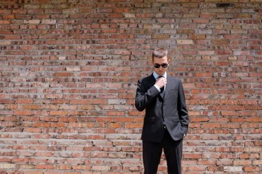 genç adam siyah takım elbise, kravat ve tuğla duvar arka plan üzerinde siyah güneş gözlüğü 