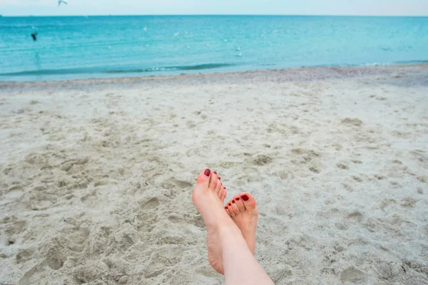 Женские ноги с красными ногтями на фоне морского берега — стоковое фото