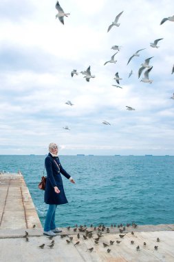 sarışın kadın martılar bulutlu sonbahar günü deniz kıyısında besleme. 
