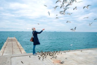 sarışın kadın martılar bulutlu sonbahar günü deniz kıyısında besleme. 