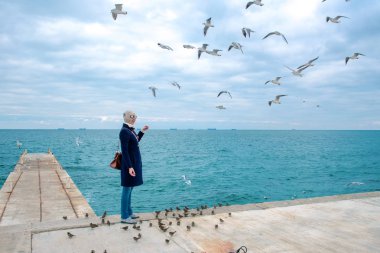 sarışın kadın martılar bulutlu sonbahar günü deniz kıyısında besleme. 
