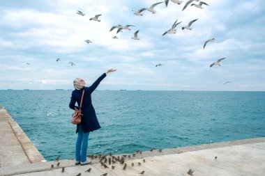 sarışın kadın martılar bulutlu sonbahar günü deniz kıyısında besleme. 