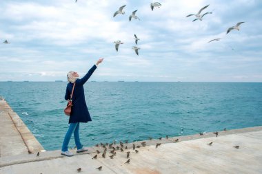 sarışın kadın martılar bulutlu sonbahar günü deniz kıyısında besleme. 