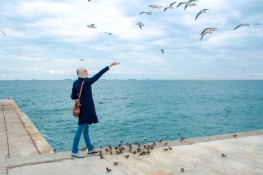 sarışın kadın martılar bulutlu sonbahar günü deniz kıyısında besleme. 