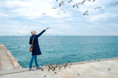 sarışın kadın martılar bulutlu sonbahar günü deniz kıyısında besleme. 