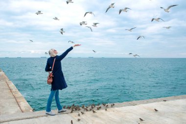 sarışın kadın martılar bulutlu sonbahar günü deniz kıyısında besleme. 