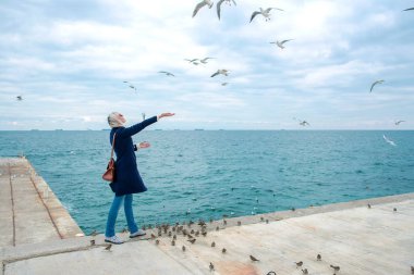 sarışın kadın martılar bulutlu sonbahar günü deniz kıyısında besleme. 