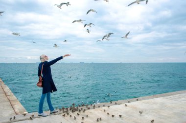 sarışın kadın martılar bulutlu sonbahar günü deniz kıyısında besleme. 