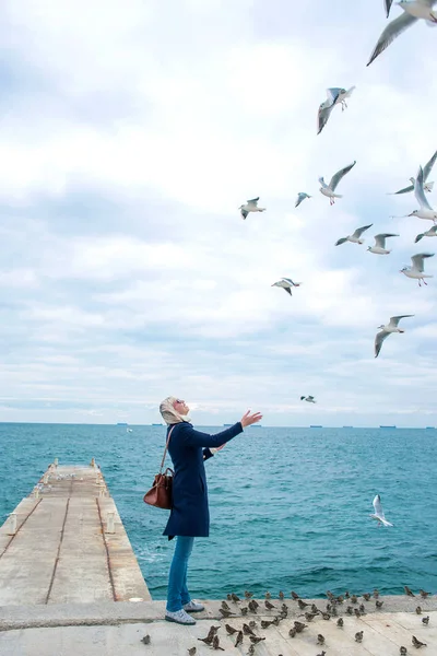 Blonde vrouw meeuwen in bewolkte herfstdag voeding aan de kust van de zee — Stockfoto