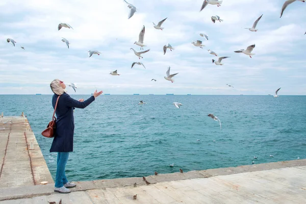 Blonde vrouw meeuwen in bewolkte herfstdag voeding aan de kust van de zee — Stockfoto