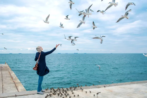 sarışın kadın martılar bulutlu sonbahar günü deniz kıyısında besleme. 