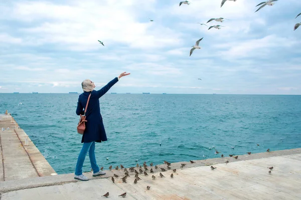 Femme blonde nourrissant les mouettes dans un jour nuageux d'automne sur la côte de la mer — Photo