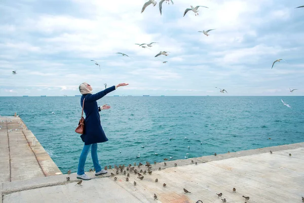 Blonde Frau füttert Möwen an bewölkten Herbsttagen an der Küste — Stockfoto