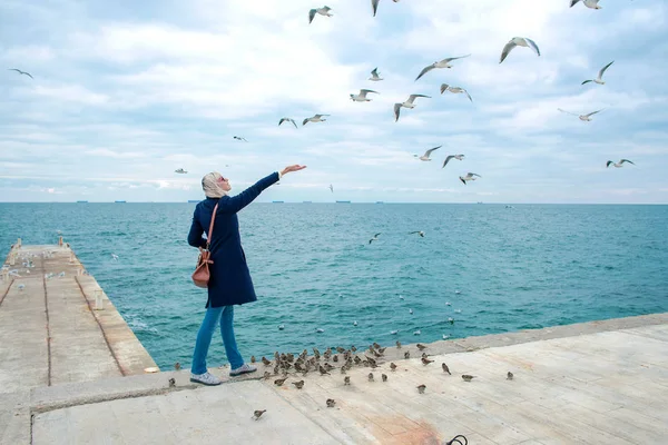 Blonde vrouw meeuwen in bewolkte herfstdag voeding aan de kust van de zee — Stockfoto