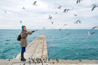 Martılar bulutlu sonbahar günü deniz kıyısında besleme kadın 