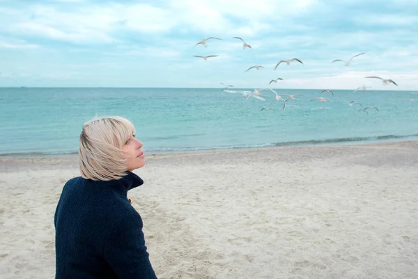 Femme blonde et mouettes dans la journée nuageuse d'automne sur la côte de la mer — Photo