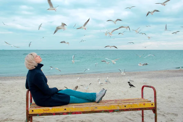 Blonde woman and seagulls in cloudy autumn day on the sea coast — Stock Photo, Image