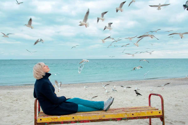 Femme blonde et mouettes dans la journée nuageuse d'automne sur la côte de la mer — Photo