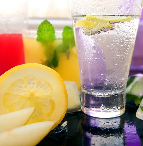 Different kinds of fresh lemonades in glasses and glass of water with lemon on light background — Stock Photo, Image