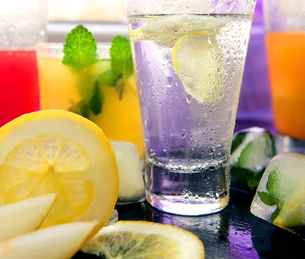Different kinds of fresh lemonades in glasses and glass of water with lemon on light background — Stock Photo, Image