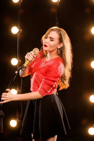 Giovane smiley bella capelli lunghi in maglione rosso ragazza con microfono canto sul palco in karaoke — Foto Stock