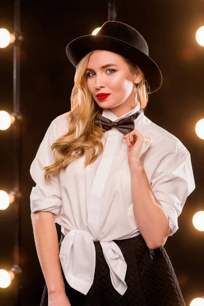 Jonge blonde aantrekkelijke vrouw in wit overhemd, vlinder, zwarte hoed op donkere achtergrond — Stockfoto
