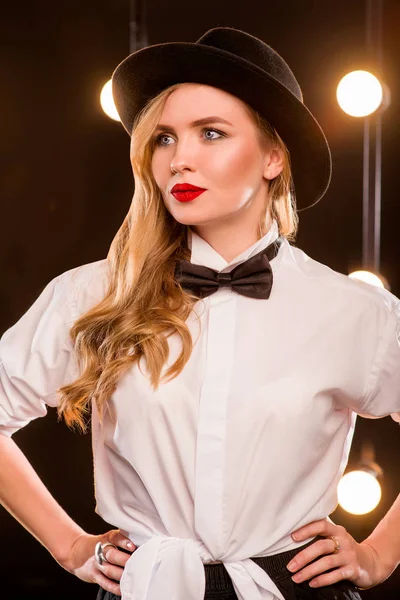 Ung blond attraktiv kvinna i vit skjorta, fjäril, svart hatt på mörk bakgrund — Stockfoto